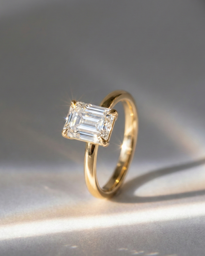 Emerald Cut Diamond Solitaire Ring — large emerald-cut diamond in yellow gold solitaire setting, editorial shot with dramatic raking light — Stone Symphony