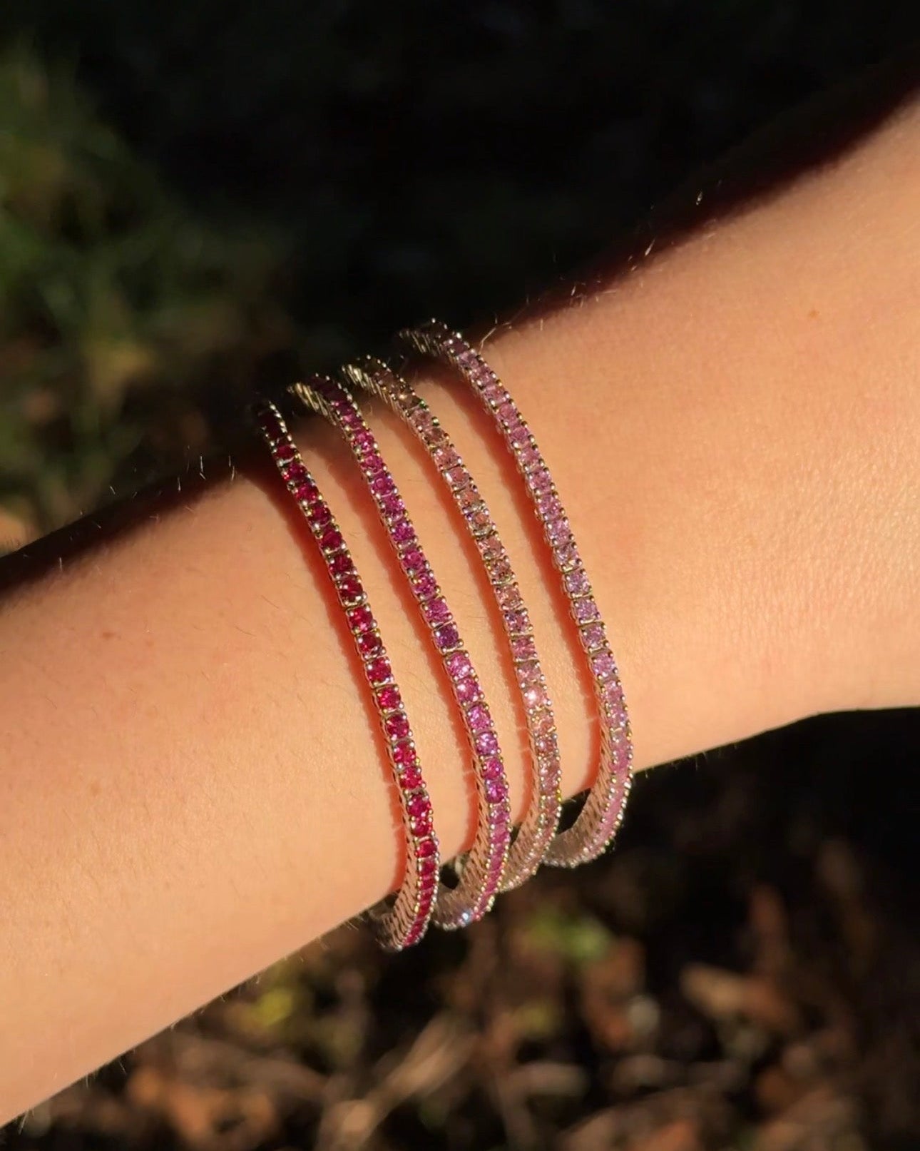 Lucie Round Tennis Bracelet — four coloured stone tennis bracelets stacked on wrist in red-to-pink gradient, outdoor lifestyle — Stone Symphony
