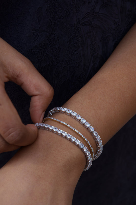 Seraphina Oval Tennis Bracelet stacked on wrist — oval-cut stones in sterling silver, editorial shot against draped silver fabric — Stone Symphony
