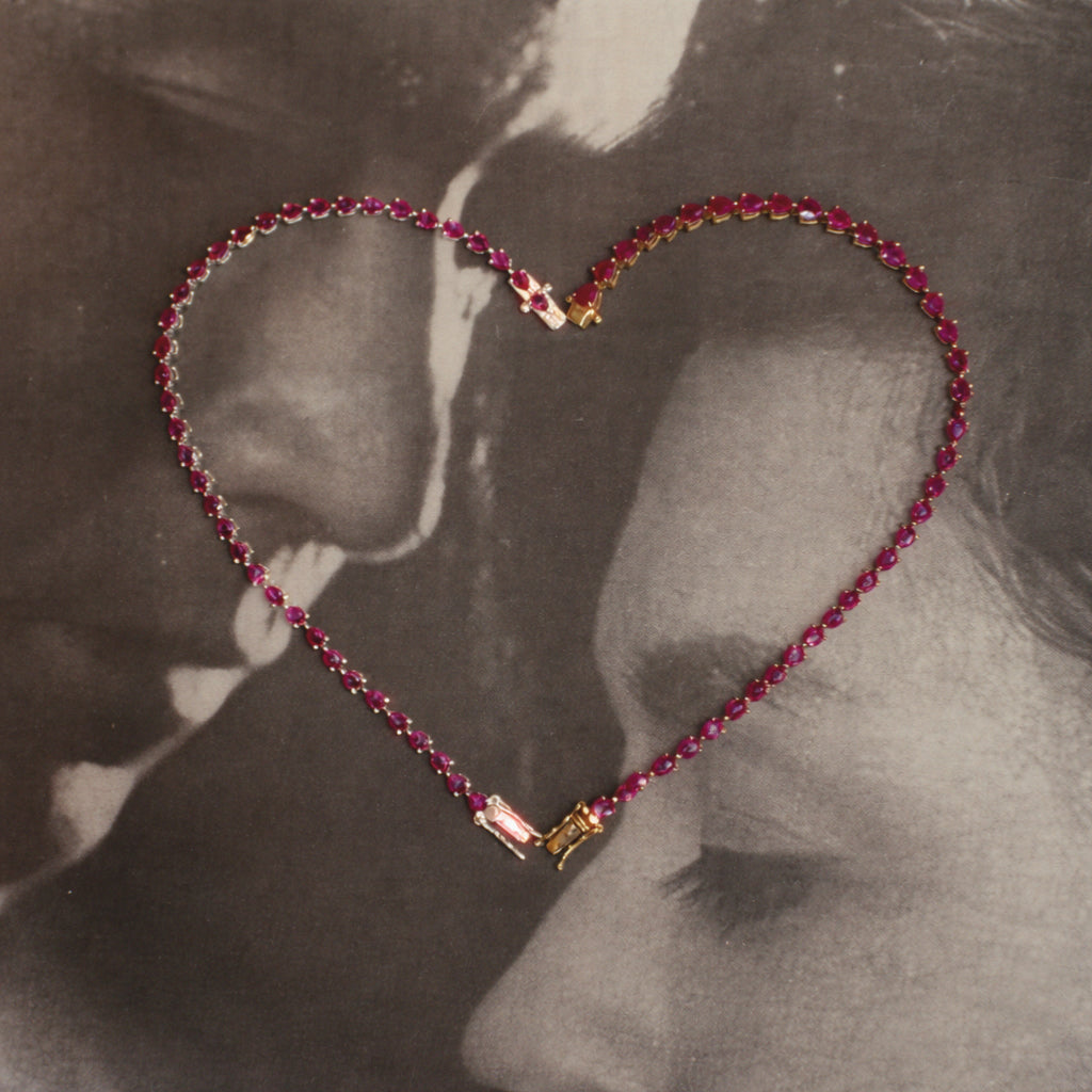 Dewdrop Ruby Tennis Bracelet arranged in heart shape — pear-drop ruby stones, romantic editorial over vintage couple photo — Stone Symphony