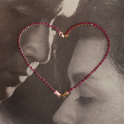 Dewdrop Ruby Tennis Bracelet arranged in heart shape — pear-drop ruby stones, romantic editorial over vintage couple photo — Stone Symphony